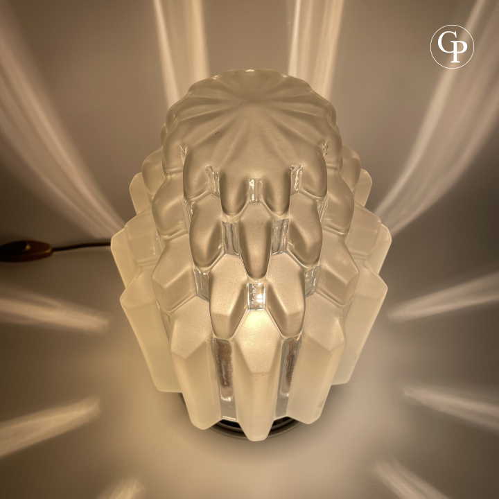 Top view of the glowing Art Deco "Skyscraper" table lamp showing the intricate geometric stepped pattern and radiating light from the frosted glass shade | Vue de dessus de la lampe de table Art Déco "Skyscraper" allumée, mettant en valeur le motif géométrique à étages et la lumière rayonnante de l’abat-jour en verre dépoli