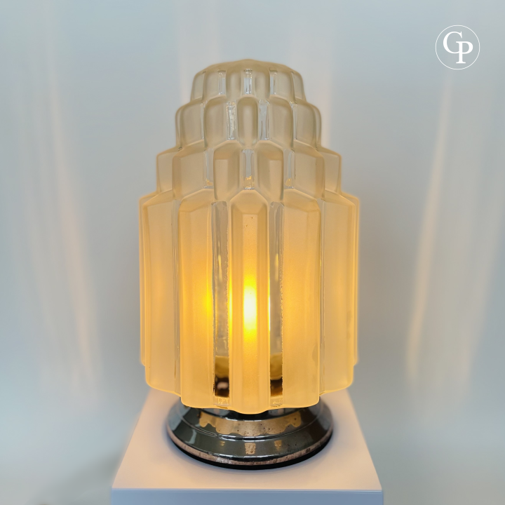 Vintage Art Deco "Skyscraper" table lamp illuminated with a warm golden glow, highlighting the beautiful tiered frosted glass shade and chrome base | Lampe de table vintage Art Déco "Skyscraper" illuminée d’une douce lueur dorée, mettant en valeur l’abat-jour en verre dépoli à étages et la base chromée