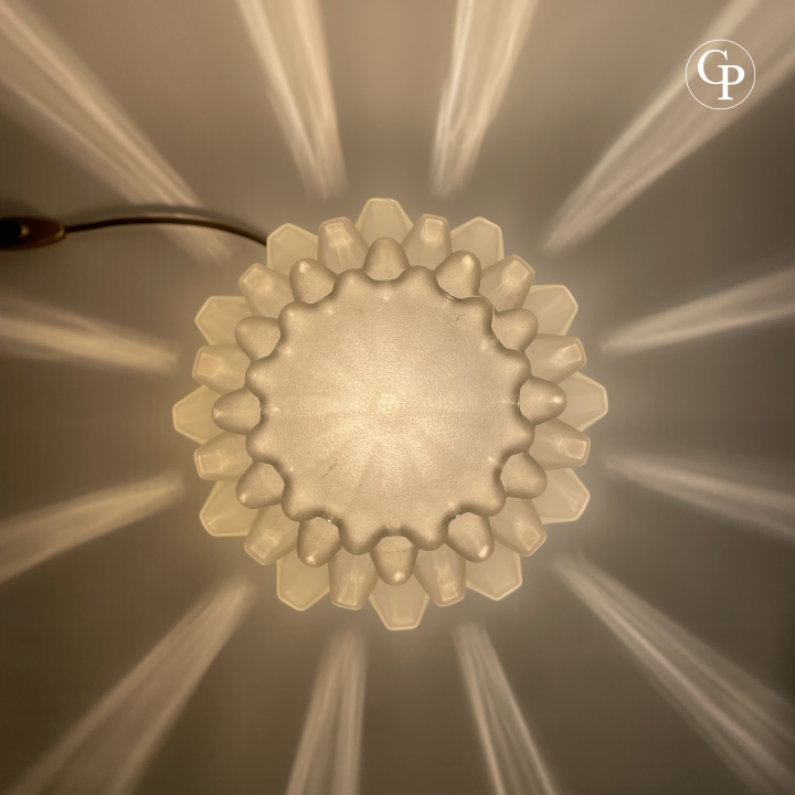 Close-up detail of the geometric stepped frosted glass shade of a vintage Art Deco table lamp with warm backlighting | Gros plan détaillé de l’abat-jour en verre dépoli à motif géométrique à étages d’une lampe de table vintage Art Déco avec rétroéclairage chaud