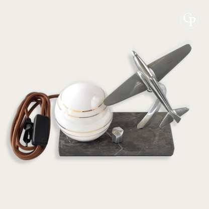 Top view of an Art Deco table lamp with chrome airplane, striped glass globe, and vintage brown fabric cable | Vue de dessus d'une lampe de table Art Déco avec avion en chrome, globe en verre rayé et câble vintage en tissu marron