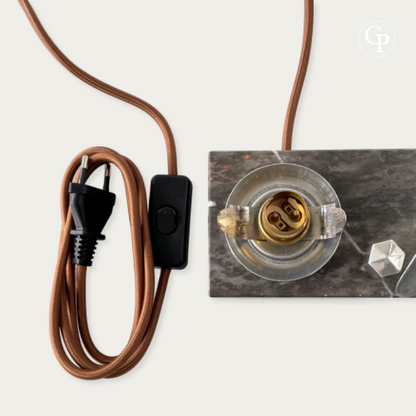 English: Close-up of the rewired and safety-compliant electrical components of the Art Deco Caudron Simoun lamp: brass bayonet socket, new brown textile cable, European plug and inline switch on the marble base. | French: Gros plan des composants électriques remis aux normes de sécurité de la lampe Art Déco Caudron Simoun : douille baïonnette laiton, nouveau câble textile brun, prise européenne et interrupteur sur la base en marbre.