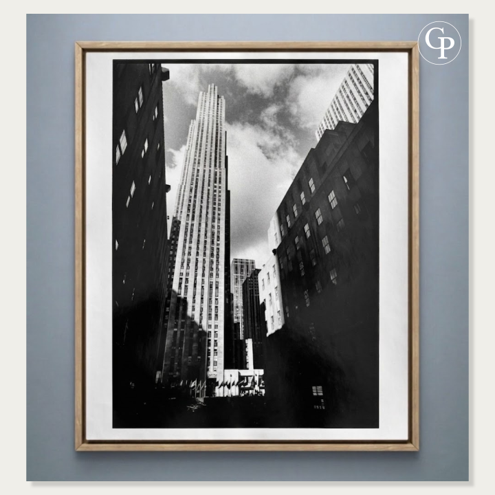 Photographie d’art en noir et blanc Rockefeller Center de Michel Pinel, tirage argentique original de 1986 présenté dans un cadre élégant en bois naturel clair sur un fond bleu gris. | Black and white art photography Rockefeller Center by Michel Pinel, original 1986 silver gelatin print displayed in an elegant light natural wood frame against a blue-grey background.