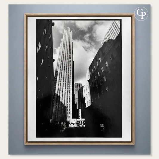 Photographie d’art en noir et blanc Rockefeller Center de Michel Pinel, tirage argentique original de 1986 présenté dans un cadre élégant en bois naturel clair sur un fond bleu gris. | Black and white art photography Rockefeller Center by Michel Pinel, original 1986 silver gelatin print displayed in an elegant light natural wood frame against a blue-grey background.