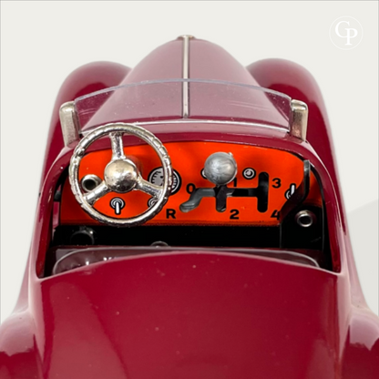 Close-up of the Schuco Examico 4001 vintage toy car cockpit, showcasing the bright orange lithographed dashboard, chrome steering wheel, and the 4-speed H-pattern gear shifter on a light background. | Gros plan sur l'habitacle de la voiture miniature Schuco Examico 4001, mettant en valeur le tableau de bord orange lithographié, le volant chromé et le levier de vitesse avec sa grille à 4 rapports.