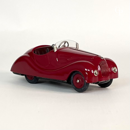 Front right three-quarter view of the deep red Schuco Examico 4001 vintage tinplate roadster toy car, showcasing its front grille, headlights, and windshield on a light background. | Vue avant droite de trois-quarts de la voiture automate Schuco Examico 4001 de couleur bordeaux, mettant en valeur sa calandre, ses phares et son pare-brise sur fond clair.