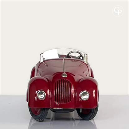 Front view of a vintage Schuco Examico 4001 clockwork roadster toy car in deep red, showing its grille, headlights, and steering wheel on a light background. | Vue de face d'une voiture automate Schuco Examico 4001 de couleur bordeaux, mettant en valeur sa calandre, ses phares et son volant sur fond clair.
